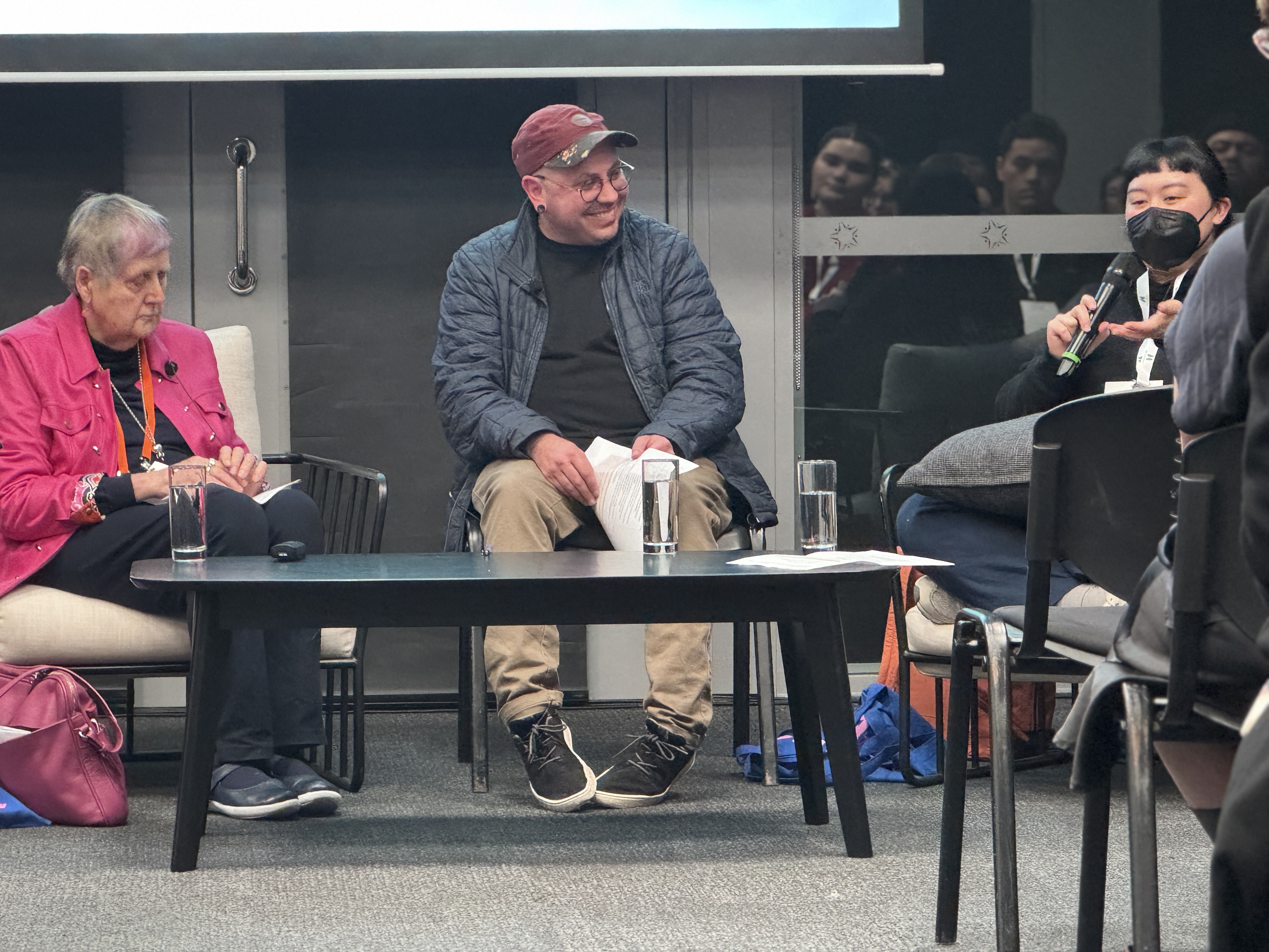 From left: Robyn, Stace and Kim talk in front of a large crowd during their session at Nui te Kōrero. In the image, Kim is speaking into a microphone while Stace and Robyn look on.